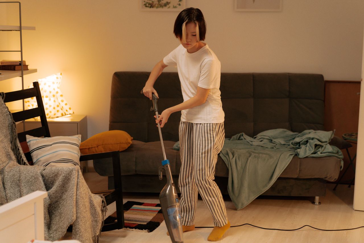 services-02 An Asian woman tidies a cluttered living room at home with a vacuum cleaner, making the space neat and orderly.
